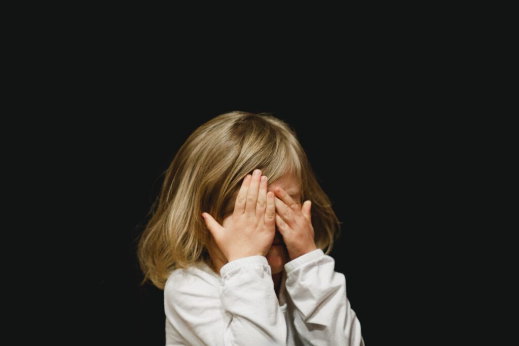Young girl on a black background with her hands covering her eyes
